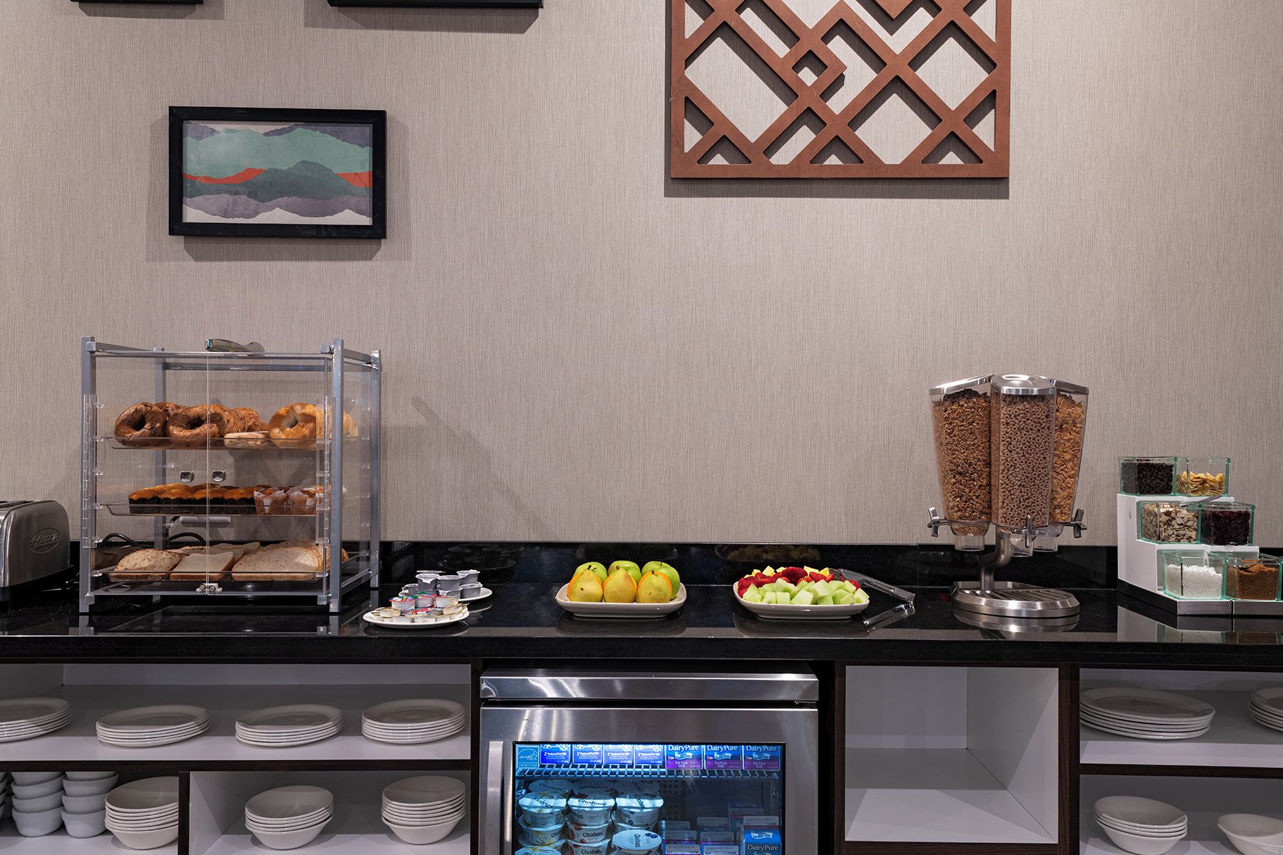 Ein Bereich mit Buffet und verschiedenen Speisen, ein Kühlschrank mit Milchprodukten sowie ein dekoratives Wandelement.