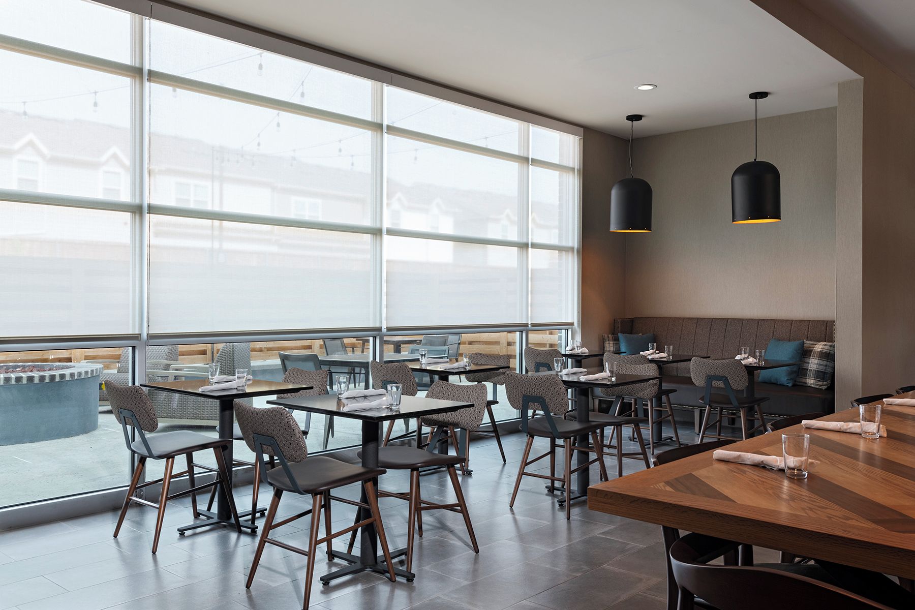A modern restaurant with high ceilings, large windows, and a mix of seating arrangements including tables and a sofa.