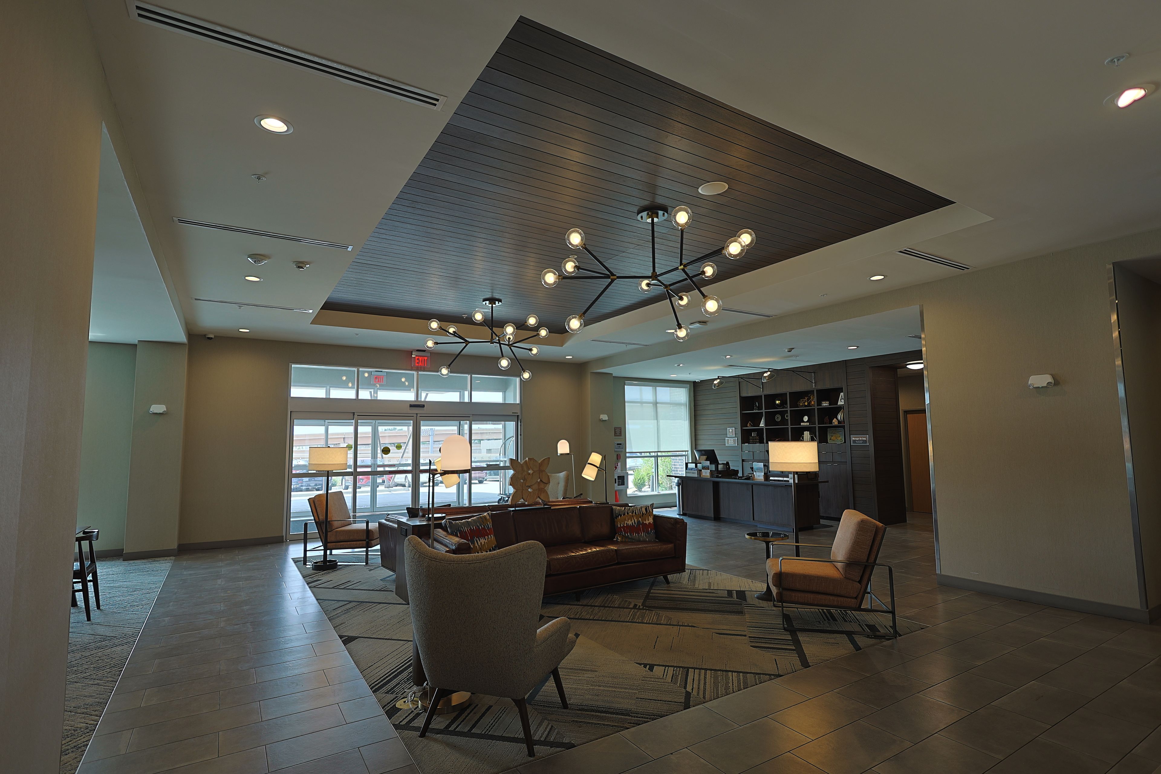 Un hall d’entrée spacieux avec un plafond haut, des luminaires modernes et un espace détente avec des canapés et des fauteuils.