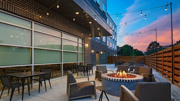 Une terrasse extérieure avec des sièges, un foyer et des guirlandes lumineuses fixées à la façade d’un bâtiment.
