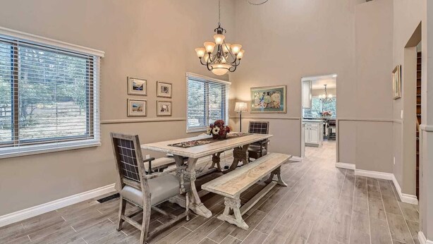 A dining area with a wooden table and benches, a chandelier, and framed artwork on the walls. - Scenic Mountainside Home with Deck and Yard (Larkspur)