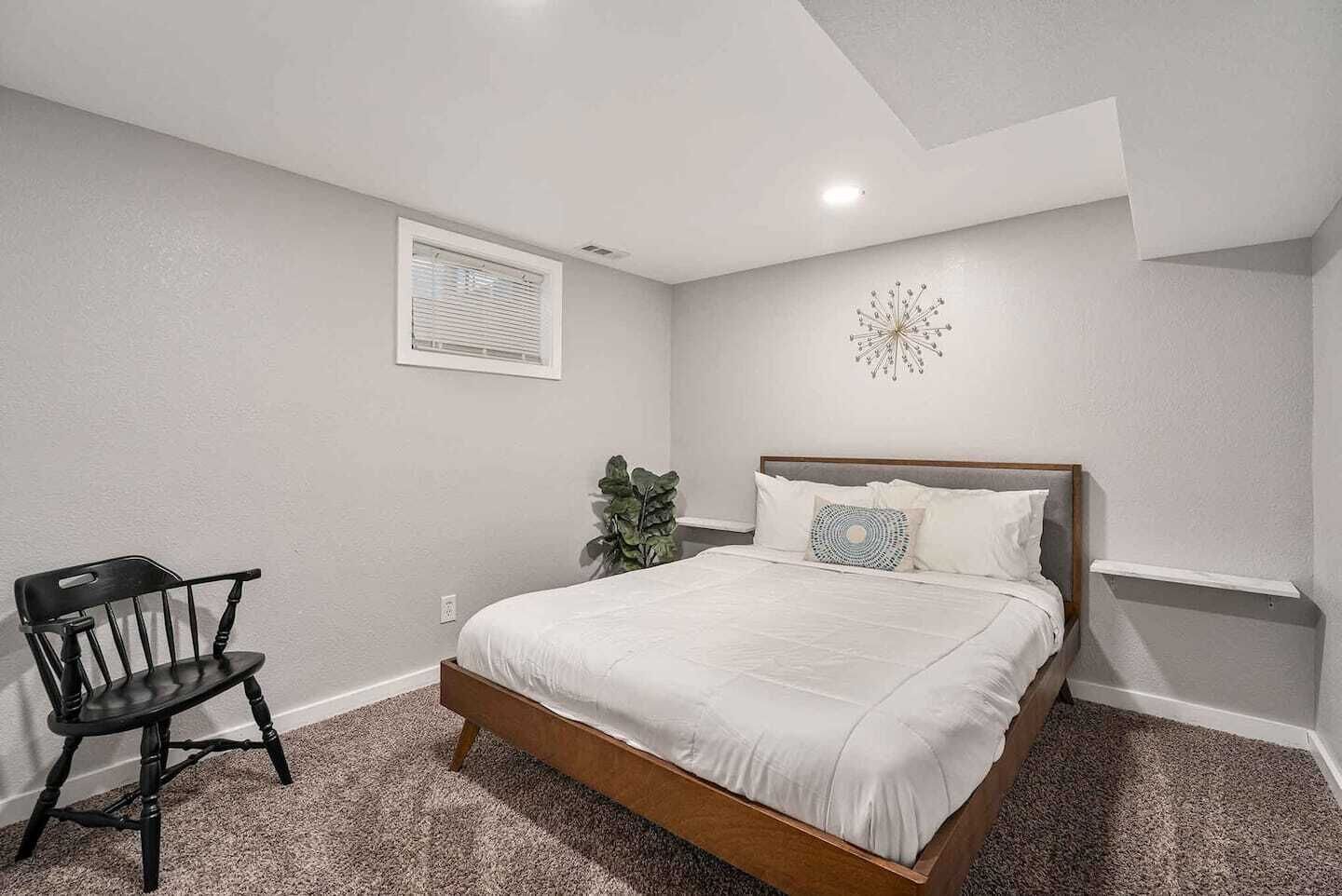 A bedroom with a bed, a chair, a plant, and a wall clock.
