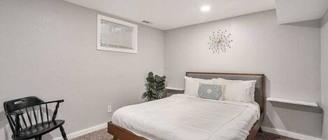 A bedroom with a bed, a chair, a plant, and a wall clock.