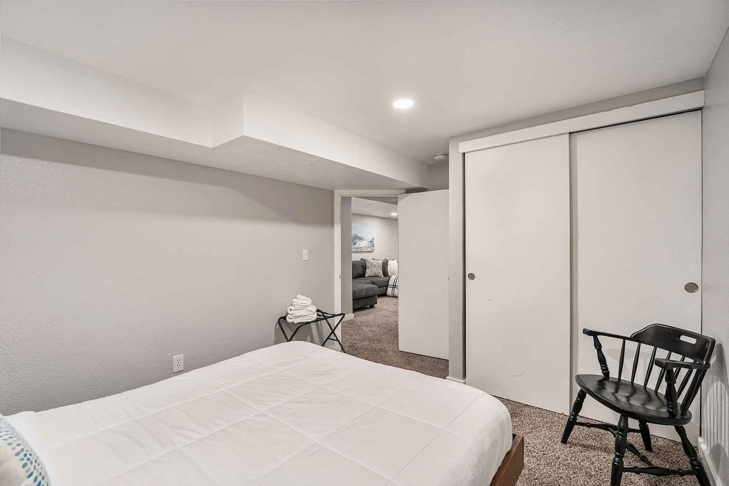 A bedroom with a bed, a chair, a closet, and a hallway leading to a living area.