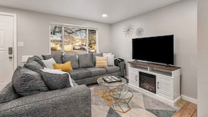 A modern living room with a sectional sofa, a flat-screen TV, and a fireplace. - Modern Retreat | Yoga Rm | Vast Yard | Near Denver (Westminster)