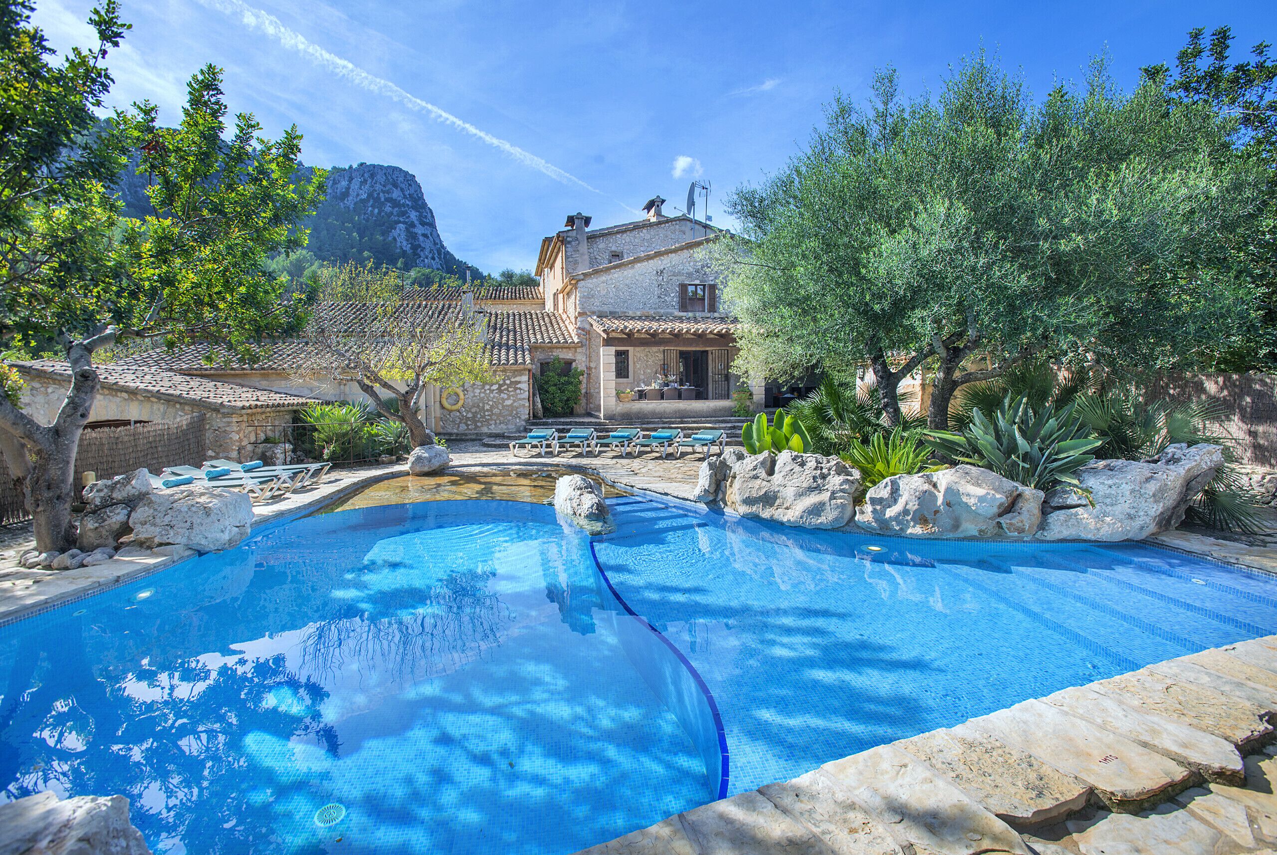 Une piscine à l’eau d’un bleu cristallin, entourée de rochers et d’arbres.
