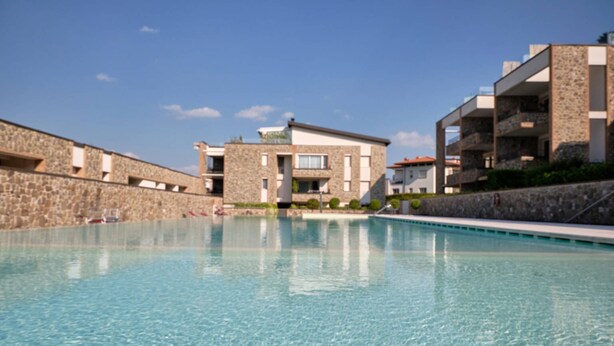 A swimming pool with a stone wall on one side and a building with a stone facade and a flat roof on the other.