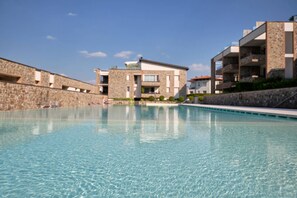 Une piscine bordée d’un côté par un mur en pierre et de l’autre par un bâtiment à la façade en pierre et au toit plat.