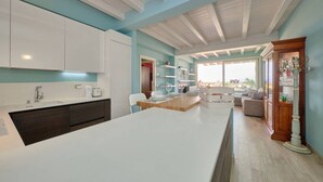 A modern kitchen with white cabinets, a large island, and a dining area with a view.