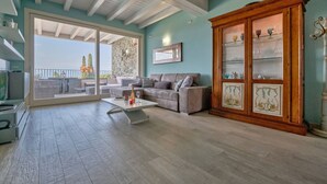 A spacious living room with a large sliding glass door leading to a balcony, a wooden cabinet with glass doors, and a modern sofa set.