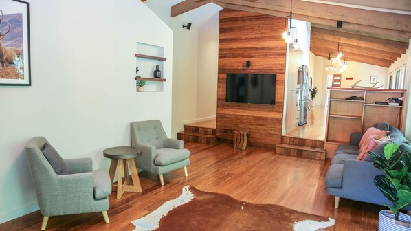 Un salon moderne avec un mur d’accent en bois, un téléviseur fixé au mur et un coin salon confortable comprenant un canapé et des fauteuils.