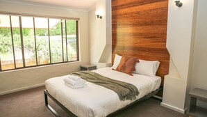 A bedroom with a bed, a nightstand, a window with blinds, and a wooden accent wall. - Haus on Houghs : Space and style in Bright (Bright)
