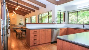 A modern kitchen with wooden cabinets, a built-in dishwasher, and large windows offering a view of greenery. - Haus on Houghs : Space and style in Bright (Bright)