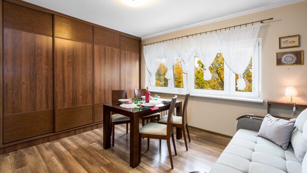 Ein Essbereich mit einem Holztisch, gedeckt für vier Personen, einer Couch und einem Fenster mit Vorhängen.