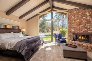 Een slaapkamer met een groot bed, een stoel, een open haard en uitzicht op de omgeving.
