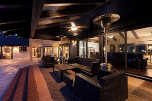Een terras buiten met rieten meubilair, plafondventilatoren en uitzicht op het interieur.