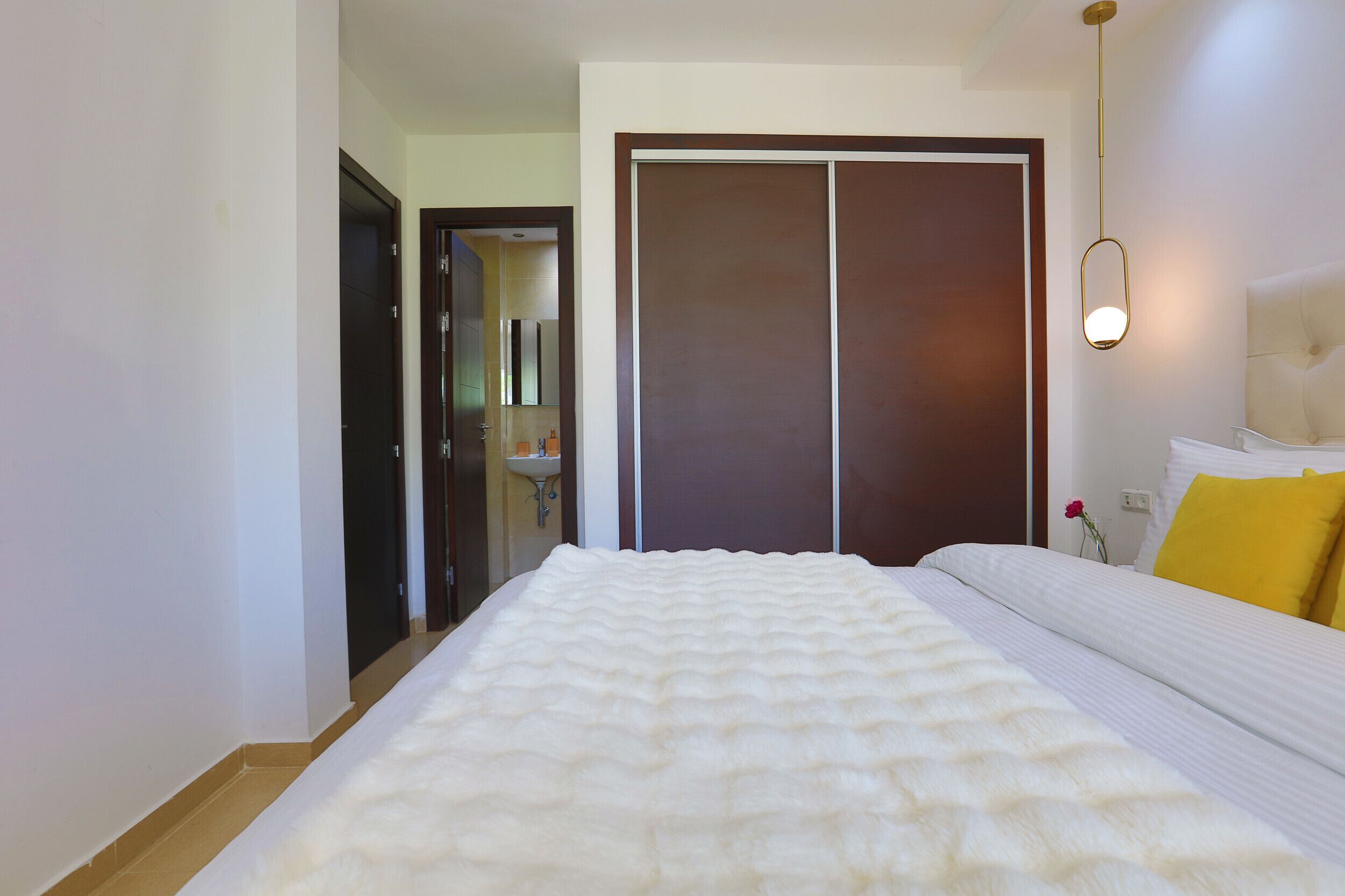 A bedroom with a large bed, a wardrobe, a bedside table, and a hanging light fixture.