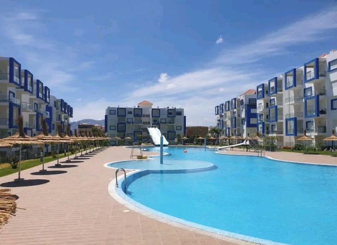 A swimming pool with a slide, surrounded by modern buildings with balconies.
