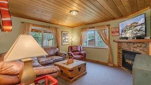 A cozy cabin interior with a wooden ceiling, leather furniture, a fireplace, and a television mounted above it. - Alpine Star Lodge (West Yellowstone)