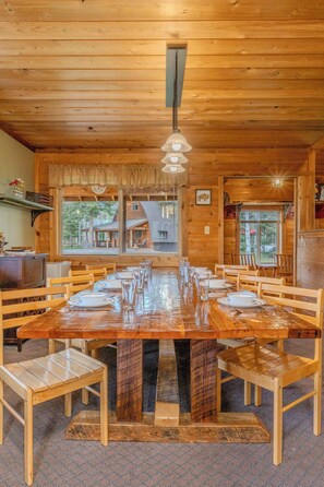 Une salle à manger en bois avec une grande table dressée pour six personnes, entourée de chaises en bois.