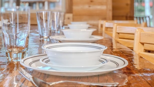A wooden interior with a long dining table set for a meal, featuring clear glassware and white plates with black stripes. - Alpine Star Lodge (West Yellowstone)