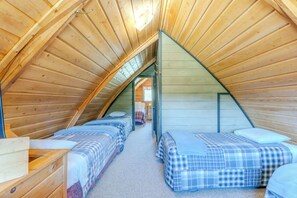 A cozy attic bedroom with wooden slats on the ceiling, two beds with plaid bedding, and a visible door leading to another room. - Blue Spruce Cabin (West Yellowstone)