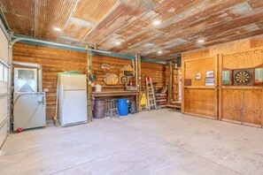 A spacious garage with a wooden ceiling, a refrigerator, a ladder, and a dartboard.