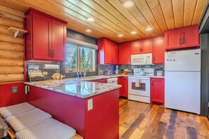 A kitchen with red cabinets, a granite countertop, a built-in oven, and a refrigerator. - Blue Spruce Cabin (West Yellowstone)