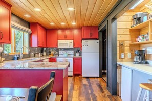 A modern kitchen with red cabinets, a central island, and wooden flooring.
