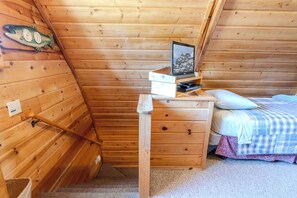 Ein gemütliches Holzblockhaus-Zimmer mit einem Bett, einer kleinen Holzkommode, einem Bilderrahmen und einer Fischdekoration an der Wand.