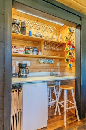 Una cocina compacta con estantes de madera, cafetera, lavamanos y refrigerador.