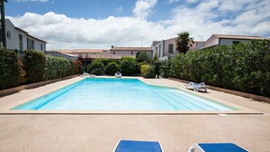 Ein rechteckiger Swimmingpool mit klarem, blauem Wasser, umgeben von einer Sandliegefläche. Liegestühle und ein kleines Boot liegen im Pool.