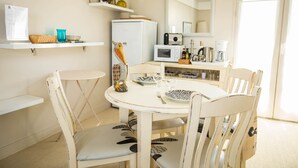 Ein Essbereich mit einem runden Tisch, weißen Stühlen, einem Kühlschrank, einer Mikrowelle und einer Kaffeemaschine.