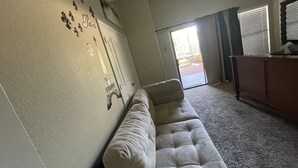 Un salón con un sofá beige, un ventanal corredero que da a un área exterior y un mueble de madera.