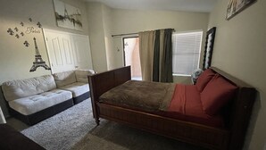 Un dormitorio con una cama, un sofá, una puerta y una ventana con cortinas.