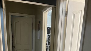 Un pasillo con una puerta blanca, un ventanal pequeño y una placa en la pared.