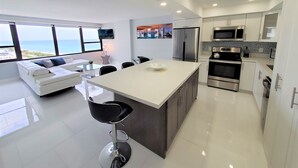 A modern kitchen with a large island, stainless steel appliances, and a view of the ocean. - Modern 3 Bedroom with Ocean Views - 1104 (Miami Beach)