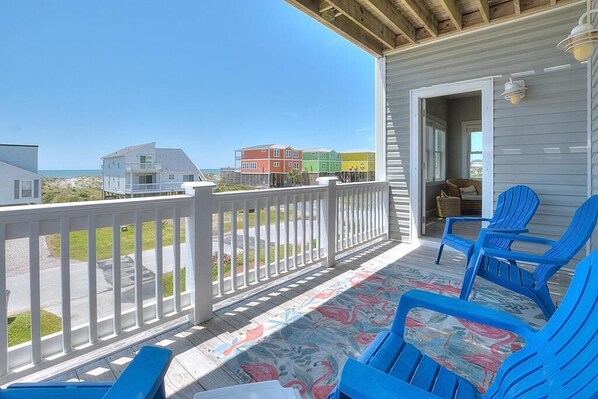 A covered porch with blue chairs, a view of colorful houses, and a wooden deck.