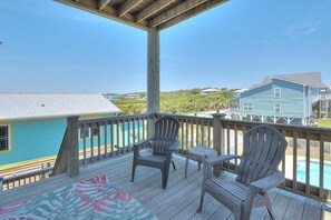 A wooden deck with two Adirondack chairs and a table, overlooking a swimming pool and houses.