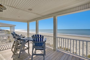 A covered deck with a view of the beach, a table, and chairs.