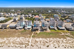 A coastal residential area with houses, some with balconies and a sandy beach in the foreground.