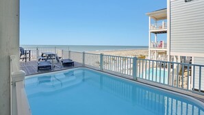 Una piscina con vista a la playa, una terraza con sillas de descanso y un edificio con balcón.