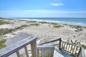 A wooden deck leading to a beach with sand dunes and ocean views.