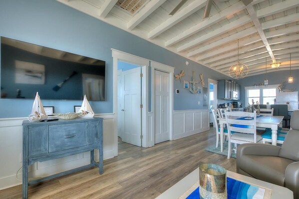 A spacious living area with a wooden floor, a dining table with chairs, and a modern kitchen in the background.