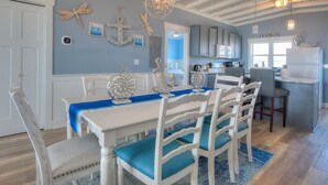 Un coin repas avec une table blanche, des coussins bleus et une décoration sur le thème de la marine.