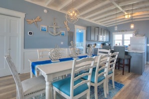 Un comedor con mesa blanca, cojines azules y decoración náutica.