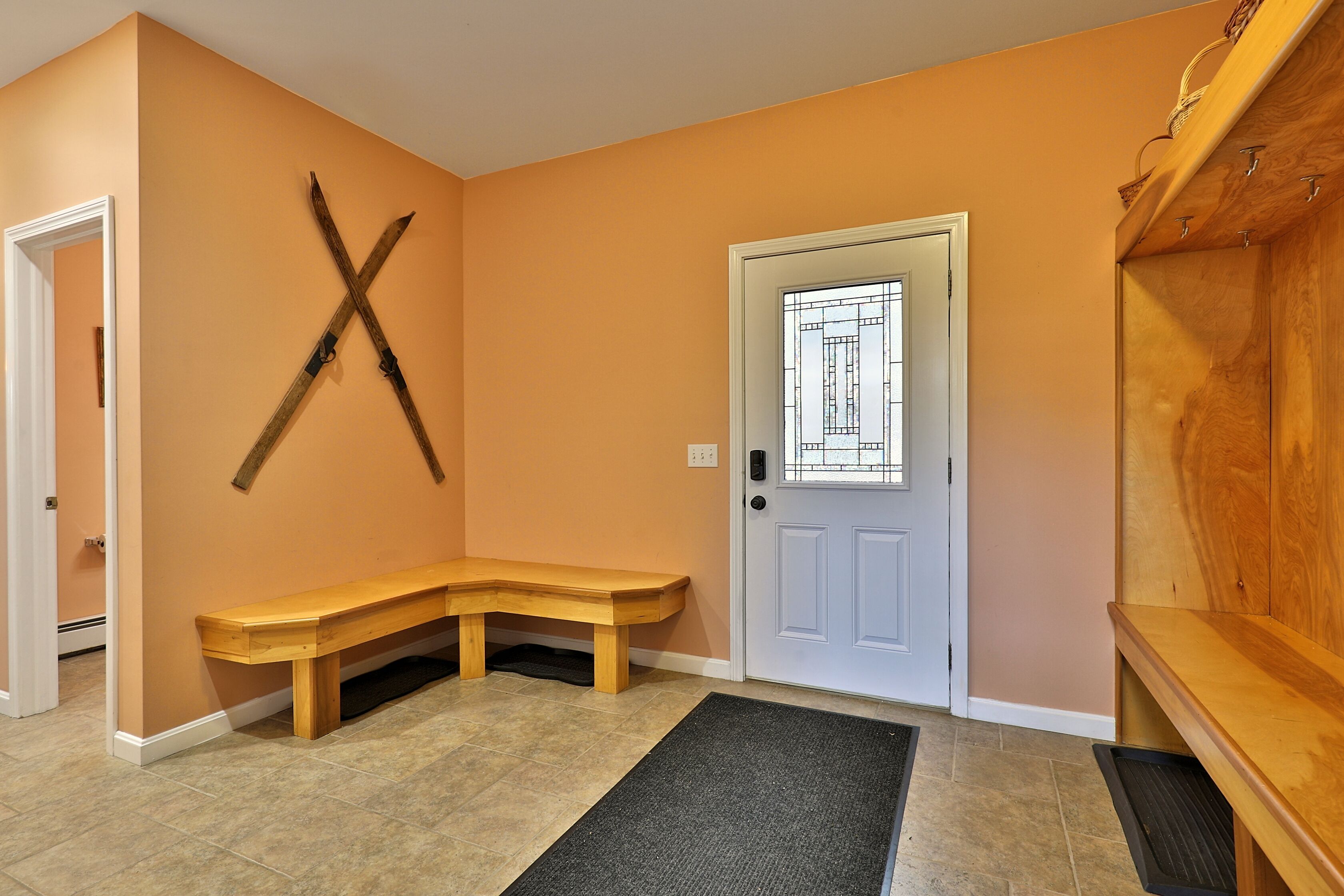 A hallway with a wooden bench, a door with a frosted glass design, and skis mounted on the wall.