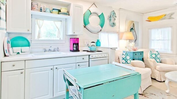 A bright kitchen with white cabinets, a teal table, and a coffee maker. - Romantic 1930s Vintage Beach Cottage Steps to Beach by Tybee Cottages (Tybee Isand)