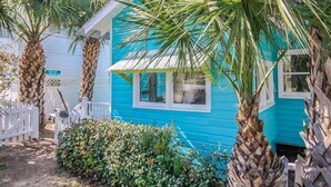 A turquoise house with a white porch, surrounded by palm trees and a white picket fence. - Romantic 1930s Vintage Beach Cottage Steps to Beach by Tybee Cottages (Tybee Isand)