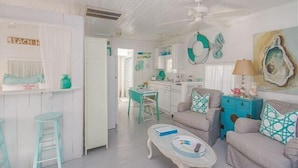 A beach-themed living room with a kitchenette, a dining area, and a view of the beach. - Romantic 1930s Vintage Beach Cottage Steps to Beach by Tybee Cottages (Tybee Isand)